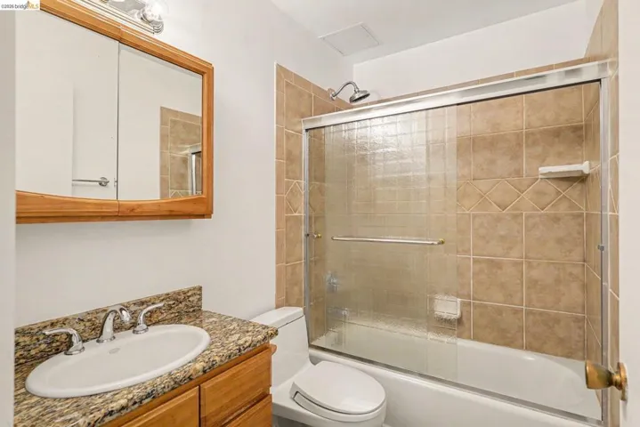Bathroom featuring a wood-finish vanity with granite-style countertop, oval undermount sink, and chrome fixtures