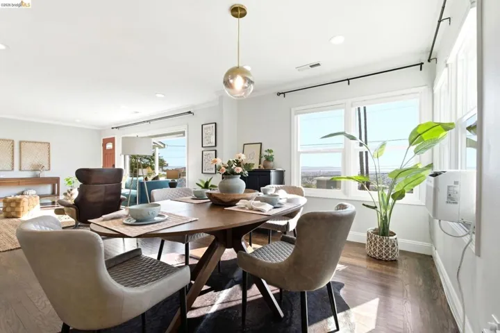 Dining area with wood-finish flooring, featuring a modern pendant light fixture and multiple windows. Hunter Douglas Electric Blinds