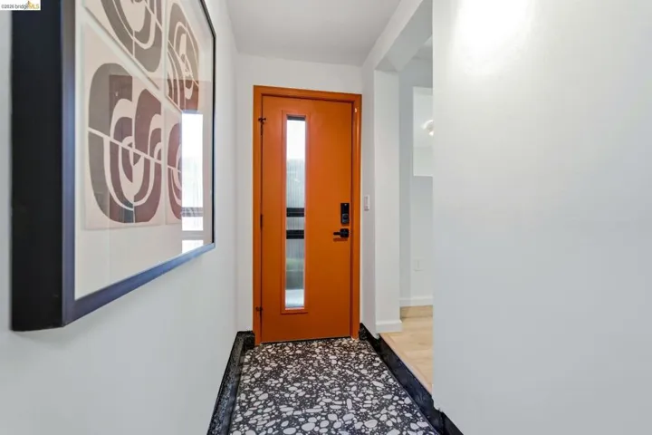 Entryway featuring a bright orange door with frosted glass inserts, a black and white speckled tile floor, and white painted walls