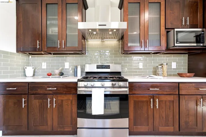 Contemporary kitchen featuring dark wood cabinetry, white countertops, a subway tile backsplash, stainless steel appliances, and under-cabinet lighting