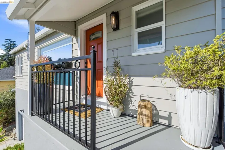 Covered front porch featuring a vibrant orange entry door with transom window, horizontal siding, and sleek black railings