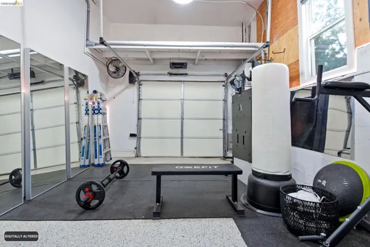 Versatile garage space featuring a roll-up door, reflective wall panels, GYM with durable rubber flooring, and a large window providing natural light and workspace.