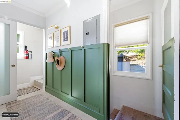 Interior hallway featuring paneling with integrated hooks, wood-finish stairs, and a window with a roller shade