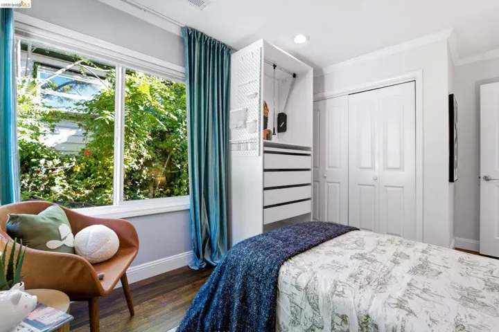Large window with green landscaping views, wood-finish flooring, custom built-in closet system with drawers, white bi-fold closet doors, and crown molding