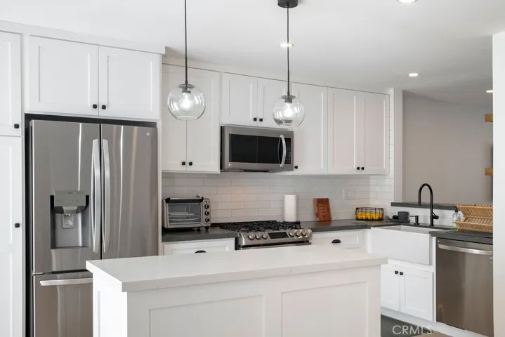 Kitchen showing included counterdepth refrigerator, quartz counters, updated tile backsplash, and Shaws farmhouse sink.