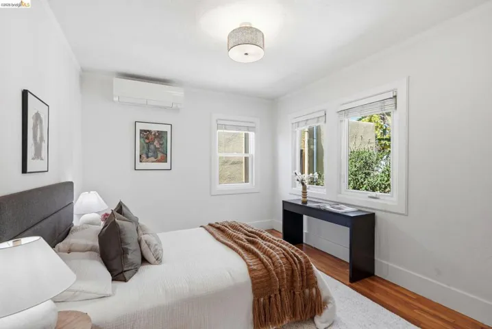 Bright room with hardwood flooring, multiple windows, a ceiling-mounted light fixture, and a wall-mounted mini-split system