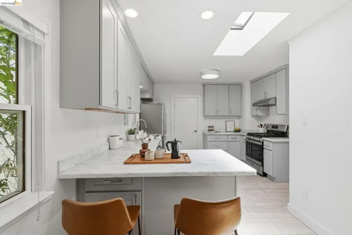 Modern kitchen featuring light gray cabinetry, white countertops, stainless steel appliances, a kitchen island, and a skylight