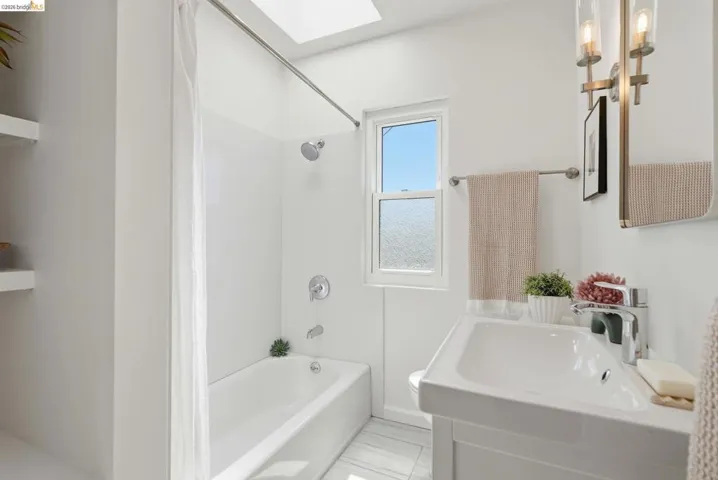 Bathroom featuring a single vanity with chrome faucet, a skylight, and a window with frosted glass