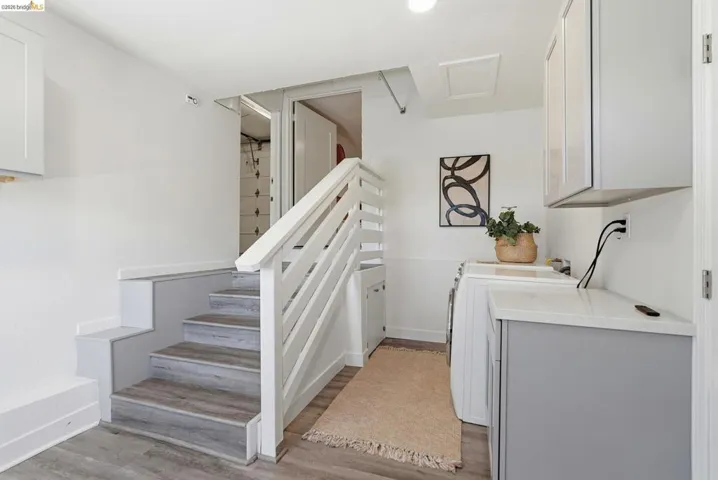 Dedicated laundry area featuring a white shaker cabinet, light countertop, and a built-in staircase with wood-finish treads and white railing