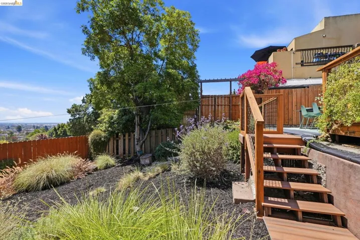 Tiered outdoor space with a natural wood staircase, elevated deck, garden beds with landscaping, and a privacy fence