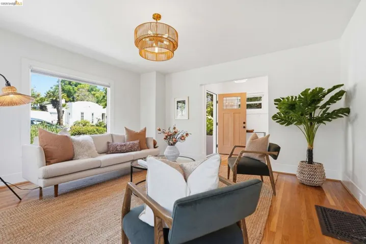 Bright living space featuring hardwood flooring, a large window, white walls, a multi-tiered woven pendant light fixture, and a wooden front entry door with glass panels