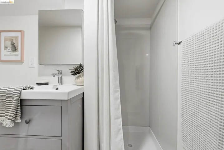 Bathroom featuring a white rectangular vessel sink, chrome faucet, gray vanity with drawer storage, mirrored medicine cabinet, and a shower with white paneling