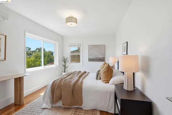 Bright bedroom with multiple windows, wood-finish flooring, and white walls