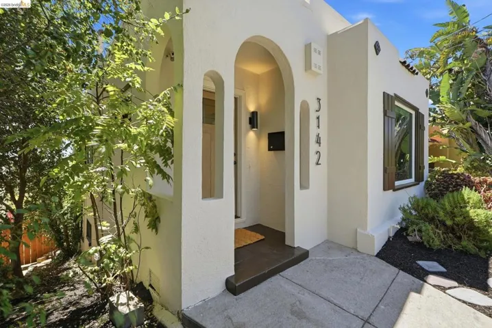 Stucco exterior featuring an arched entry, modern outdoor lighting, and contrasting dark window shutters
