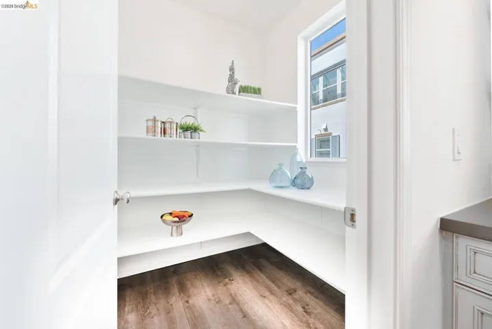 Pantry featuring extensive built-in white shelving, wood-finish flooring, and a single window