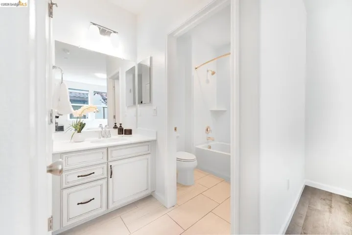 Bathroom featuring a white vanity with distressed-look cabinetry and dark hardware, set against light-toned floor tiles