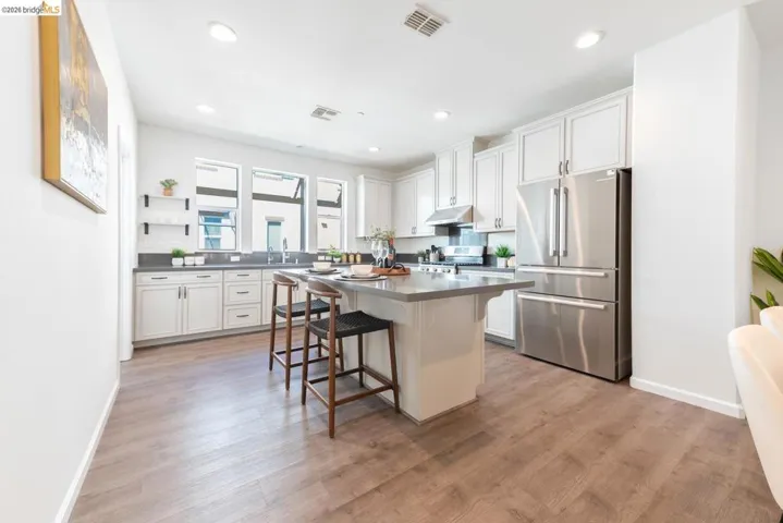 Modern kitchen featuring white cabinetry, stainless steel appliances, a center island with seating, dark countertops, and wood-finish flooring