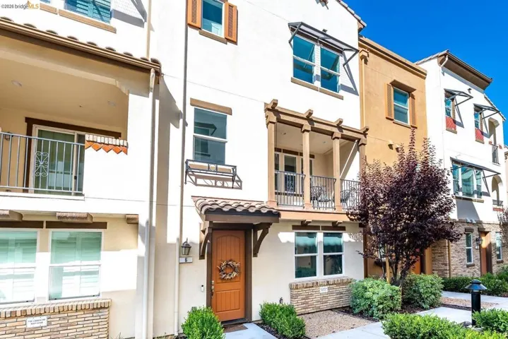 Multi-story townhome with a warm wood-toned entry door, terracotta-style roof tiles, and a decorative trellis over a second-floor balcony