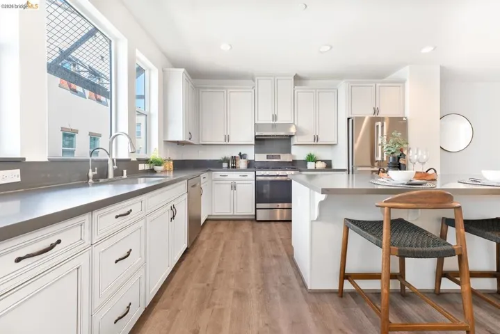 Modern kitchen featuring white shaker cabinetry, dark countertops, wood-finish flooring, stainless steel appliances, and a central island with a breakfast bar