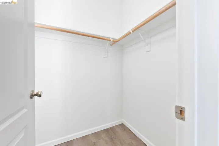 Walk-in closet with clean white walls, natural wood clothing rod, white shelving supports, white baseboards, and wood-finish flooring