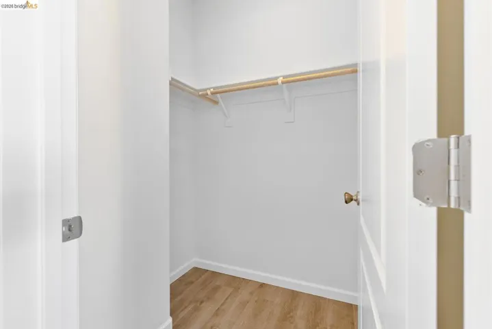Walk-in closet featuring wood-finish flooring, white baseboards, and a built-in wooden hanging rod with shelving