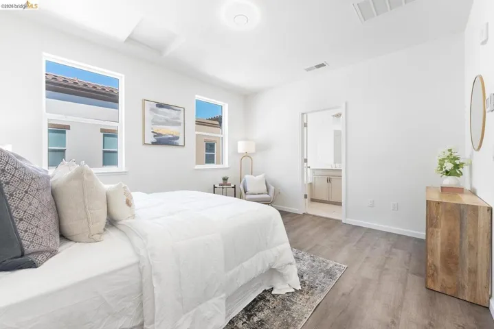 Spacious room featuring multiple windows with clean white frames, tray ceiling detail, wood-finish flooring, and an en-suite bathroom with a vanity