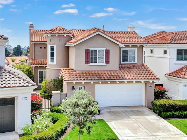 An elevated front perspective showcases the home's distinctive coastal architecture, highlighted by its elegant turret, manicured landscaping, and oversized two-car garage. Beyond the neighborhood rooftops, peek ocean and city light views hint at the exceptional setting that awaits.