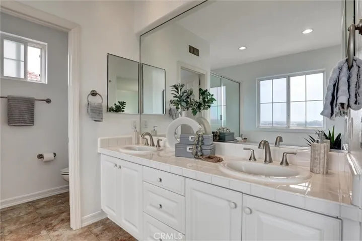 The spacious primary bathroom features dual vanities, a soaking tub, a separate shower, and breathtaking views of the Upper Newport Bay and Pacific Ocean beyond.