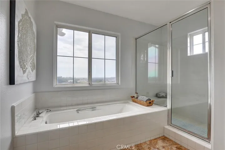 Natural light and panoramic coastal views enhance the spacious primary bathroom with its dual vanities, soaking tub, and separate shower.