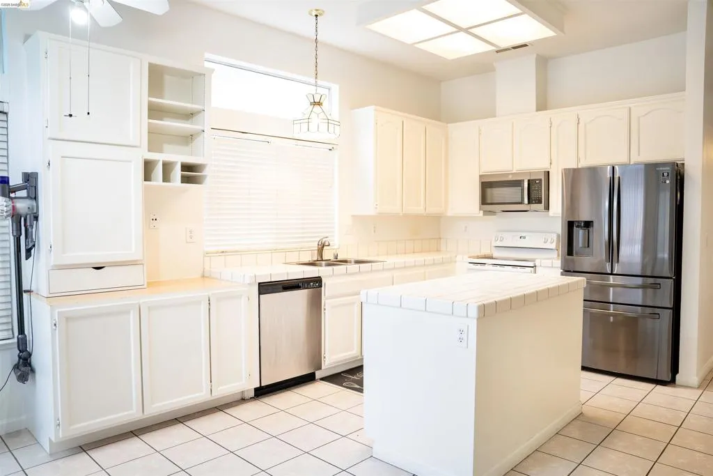 Kitchen featuring white cabinetry, tile countertops, stainless steel appliances, a central island, and tile flooring