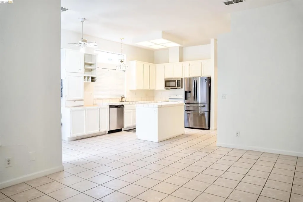 Open-concept kitchen featuring an island, tile flooring, white cabinetry, stainless steel appliances, and a ceiling fan