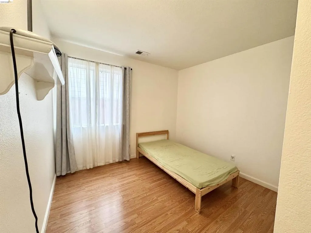 Room featuring wood-finish flooring, a window with sheer and blackout curtains, and white baseboards
