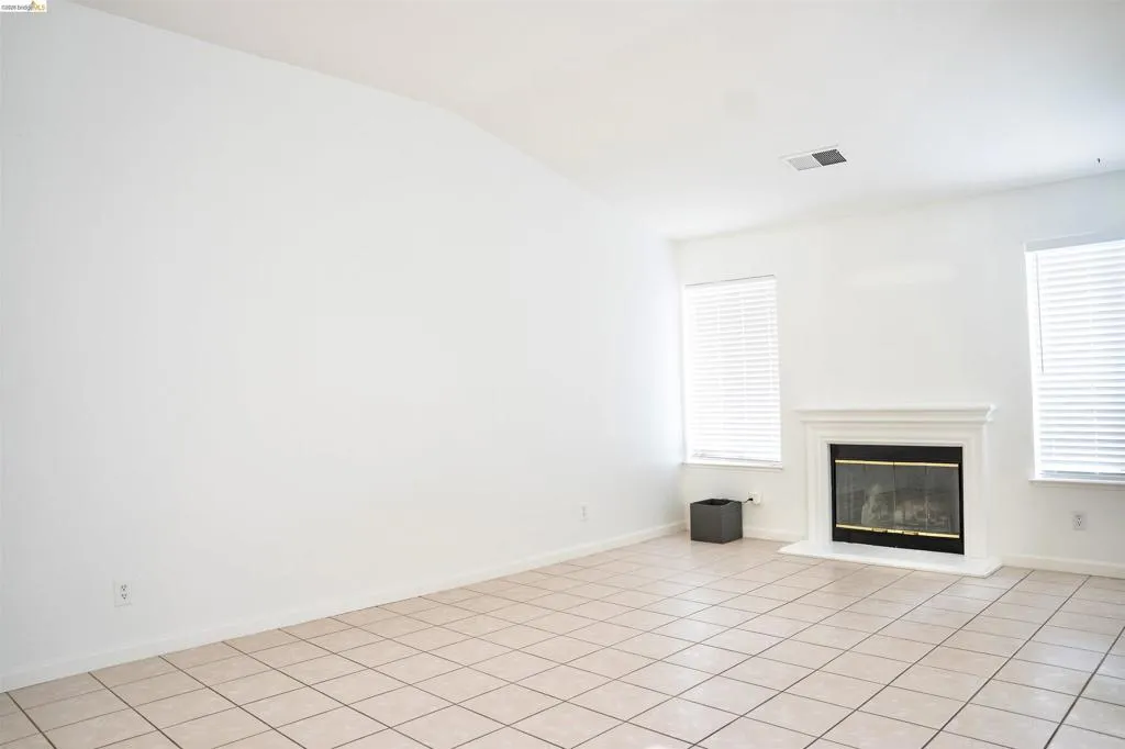 Spacious room featuring neutral tile flooring, a fireplace with a white mantel, and multiple windows with blinds