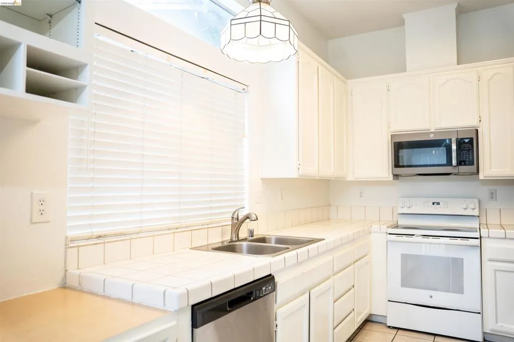 Kitchen featuring white cabinetry, tile countertops, stainless steel sink, built-in microwave, and white range
