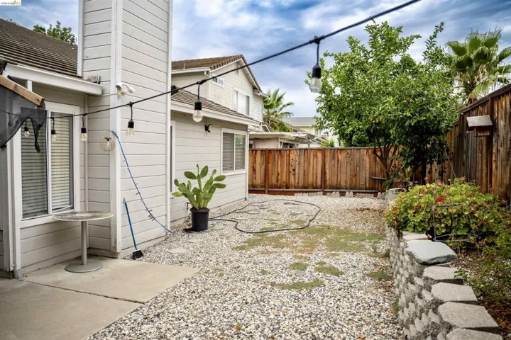 Private rear yard featuring a concrete patio, gravel landscaping, a retaining wall with planting beds, a wood privacy fence, and mature trees