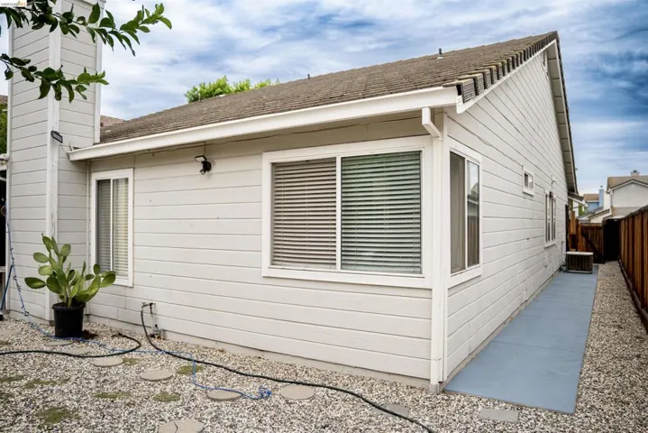 Exterior siding with white trim, multiple windows featuring horizontal blinds, and a gravel ground cover