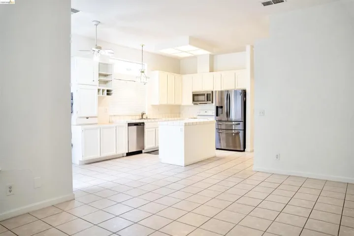 Open-concept kitchen featuring an island, tile flooring, white cabinetry, stainless steel appliances, and a ceiling fan