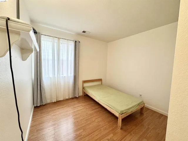 Room featuring wood-finish flooring, a window with sheer and blackout curtains, and white baseboards