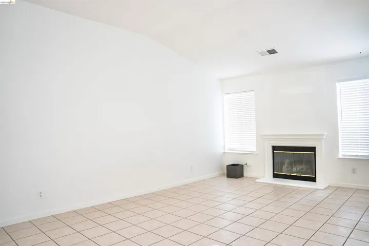 Spacious room featuring neutral tile flooring, a fireplace with a white mantel, and multiple windows with blinds