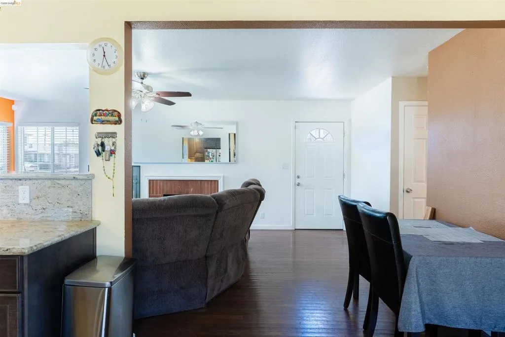 Living area with wood-finish flooring, a white front entry door with a decorative glass insert, and a ceiling fan