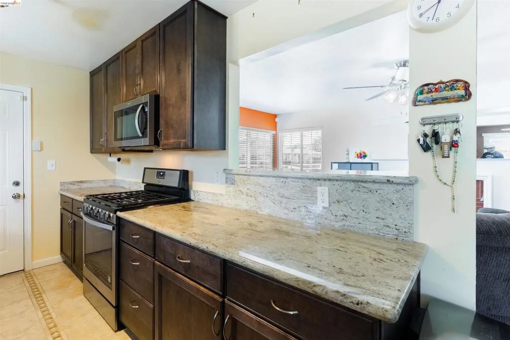 Kitchen featuring dark wood-finish cabinetry, light-toned granite countertops, and stainless steel appliances including a range and microwave