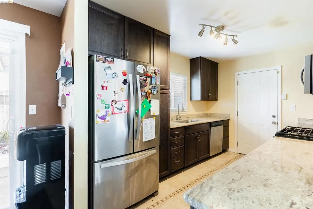 Kitchen featuring dark wood cabinetry, granite countertops, tile flooring with decorative inlay, stainless steel appliances, and track lighting