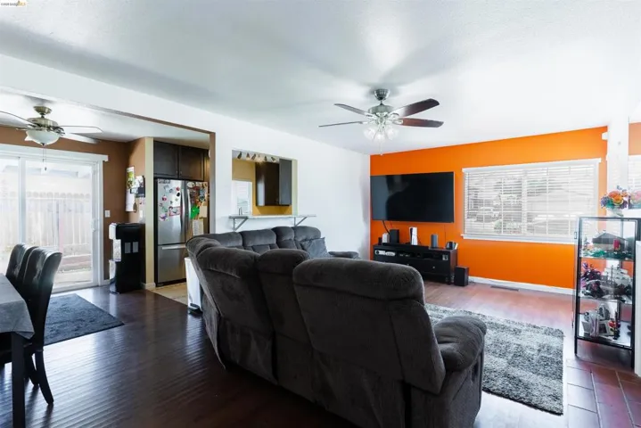 Living area featuring wood-finish flooring, a ceiling fan with integrated lighting, and a large window with blinds