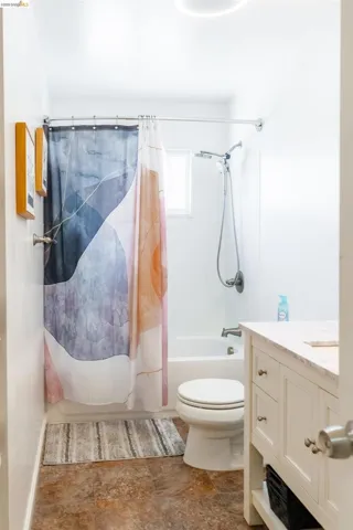 Bathroom featuring a white bathtub, shower with wall-mounted fixture, and a white vanity with a light-toned countertop