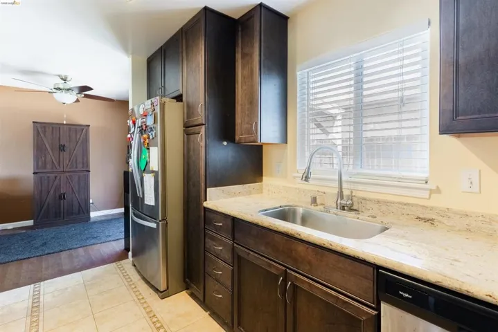 Kitchen featuring dark wood cabinetry, light-toned countertop, stainless steel sink with a gooseneck faucet, and tile flooring