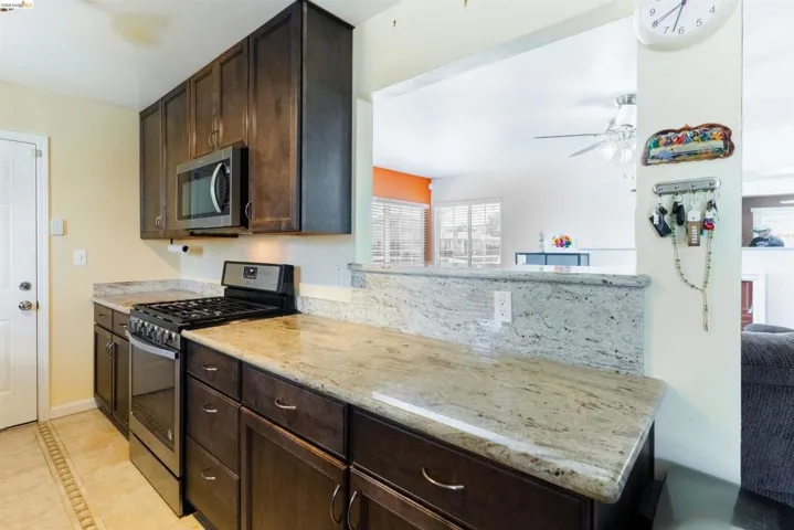 Kitchen featuring dark wood-finish cabinetry, light-toned granite countertops, and stainless steel appliances including a range and microwave