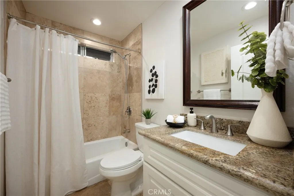 Upgraded guest bathroom featuring granite countertops, white cabinetry, and travertine finishes located upstairs.