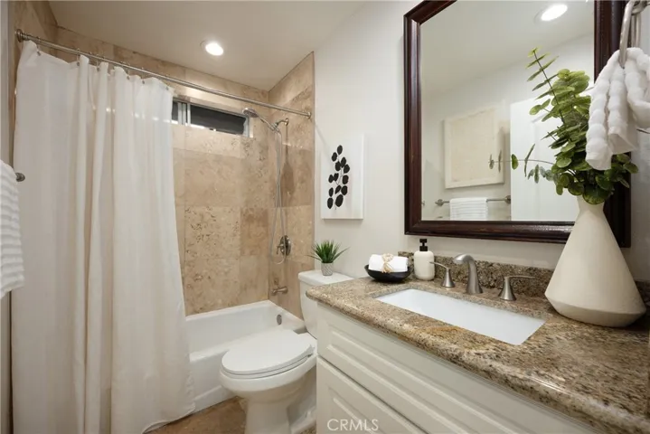 Upgraded guest bathroom featuring granite countertops, white cabinetry, and travertine finishes located upstairs.