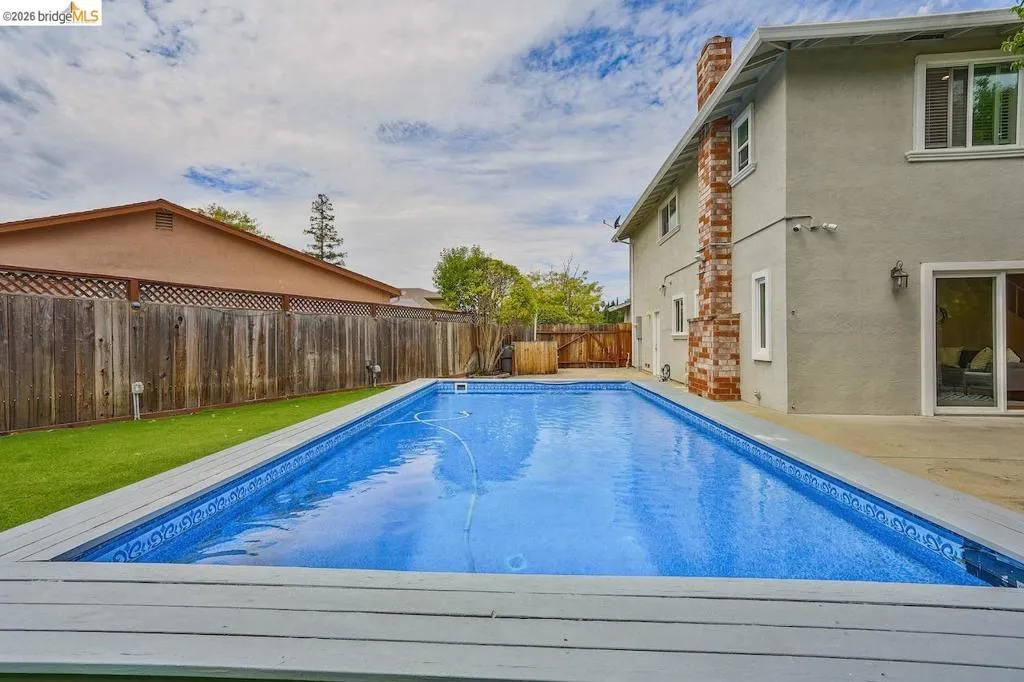 Backyard swimming pool with wood-finish decking, surrounded by a stucco exterior residence and a brick chimney