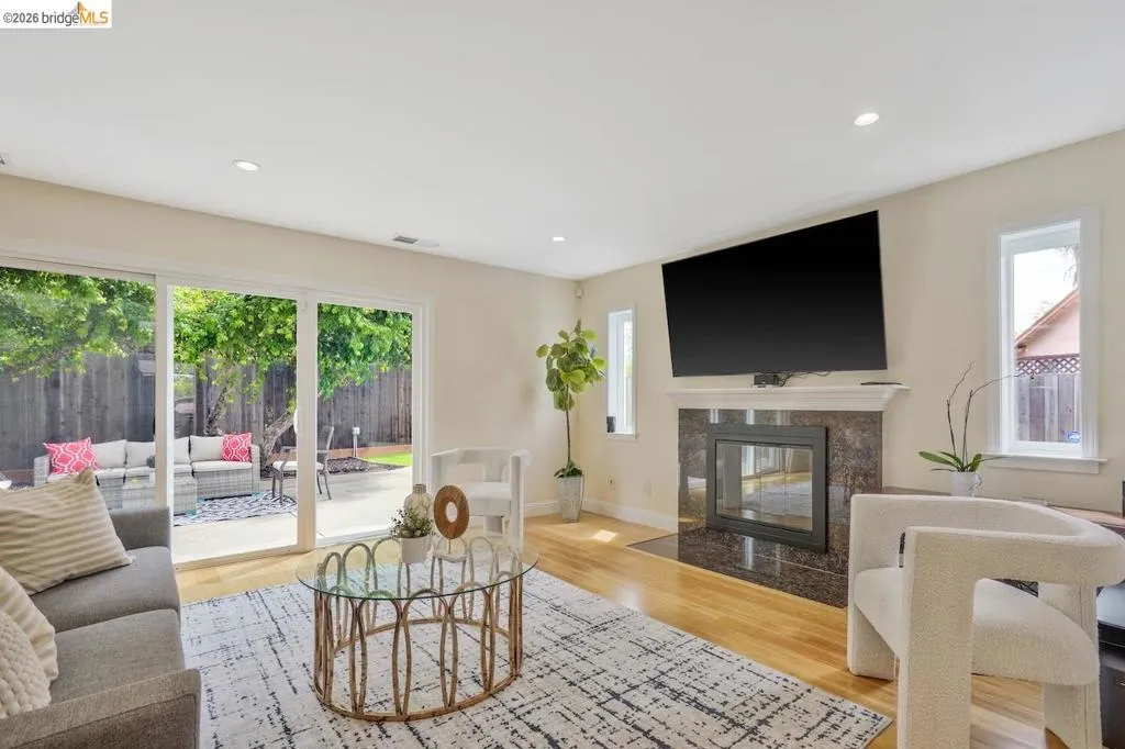Living space featuring hardwood flooring, a fireplace with a stone surround, recessed lighting, and sliding glass doors opening to a backyard patio